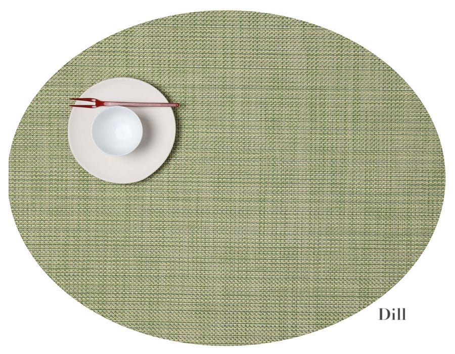 The oval green Chilewich placemat displays a white plate, bowl, and red-brown chopsticks at the top left. "Dill" is on the lower right. Easy to clean with bleach-based cleanser—perfect for any dining occasion.