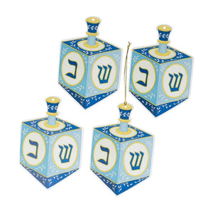 Four Caspari Dreidel Ornament Tags, each blue and yellow with Hebrew letters on every side and finished with a gold hanging cord, grouped together on a white background.