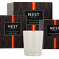 A white Nest Sicilian Tangerine Candle from the Sicilian Tangerine Candle Collection sits in front of three matching black and orange boxes.