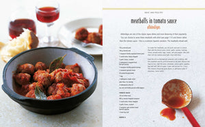 A bowl of meatballs in tomato sauce with bay leaves—a classic among Spanish appetizers—takes center stage, while a glass of red wine sits in the background and an open page from *Tapas* by Simon & Schuster showcases one of the beloved recipes for meatballs in tomato sauce.