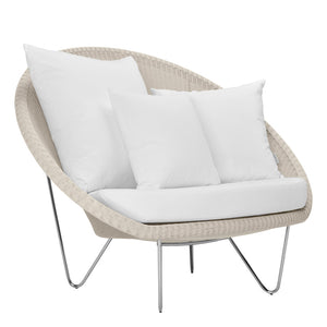The Janus et Cie Lounge Chair in Schooner Snow features a round beige wicker frame, metal legs, plush cushion, and three large white pillows—ideal for adding midcentury modern elegance to your luxury space.