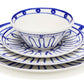 Themis Z’s Kyma Blue Dinnerware Collection, inspired by the Greek Aegean sea, features blue geometric patterns on a bowl stacked atop three plates of varying sizes, evoking tranquil blues.