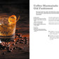 A copy of The Art & Craft of Coffee Cocktails by Simon & Schuster sits on a dark surface, flanked by an orange twist-garnished Coffee Marmalade Old Fashioned, scattered coffee beans, and a metal jigger—perfect inspiration for those eager to explore innovative cocktail recipes.