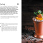 A metal cup filled with crushed ice, garnished with orange peel, mint, and cherries sits on a dark surface scattered with coffee beans and a spilled tin of ground coffee—an inviting scene that perfectly captures the creative inspiration found in The Art & Craft of Coffee Cocktails by Simon & Schuster, ideal for anyone interested in unique coffee cocktails or seeking new cocktail recipes.