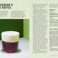 A glass of Irish coffee with a creamy foam on top sits on a dark surface next to a page of text and Simon & Schuster’s Curious Barista’s Guide To Coffee.