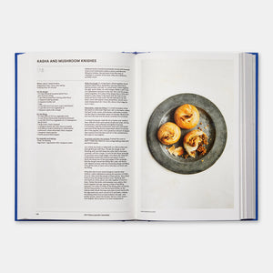 An open copy of *The Jewish Cookbook* by Phaidon highlights a recipe for "Kasha and Mushroom Knishes" on the left page, accompanied by a tempting photo of three knishes displayed on a gray plate on the right.