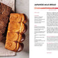 Two loaves of Japanese milk bread—one plain and one marbled with chocolate—sit side by side on a beige surface next to the open King Arthur Baking Company Big Book of Bread from Simon & Schuster, inviting you to discover new bread recipes inspired by its expert guidance.