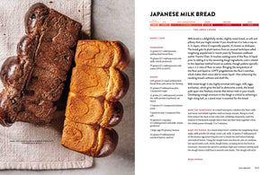 Two loaves of Japanese milk bread—one plain and one marbled with chocolate—sit side by side on a beige surface next to the open King Arthur Baking Company Big Book of Bread from Simon & Schuster, inviting you to discover new bread recipes inspired by its expert guidance.