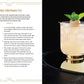 A glass of Mocktail Club by Simon & Schuster—lychee elderflower fizz served over ice and garnished with mint—rests on a reflective black surface beside a recipe page detailing ingredients and instructions, making it an appealing option for those seeking creative mocktails or inspired new mocktail recipes.