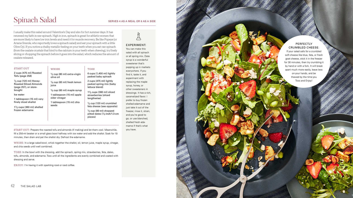 An open cookbook titled “Salad Lab: Whisk, Toss, Enjoy!” by Simon & Schuster displays a vibrant spinach salad recipe on the left page and a platter brimming with colorful spinach salad featuring strawberries, nuts, and cheese on the right—all presented with serving tongs atop a dark surface, reminiscent of The Salad Lab’s viral creations seen on TikTok.