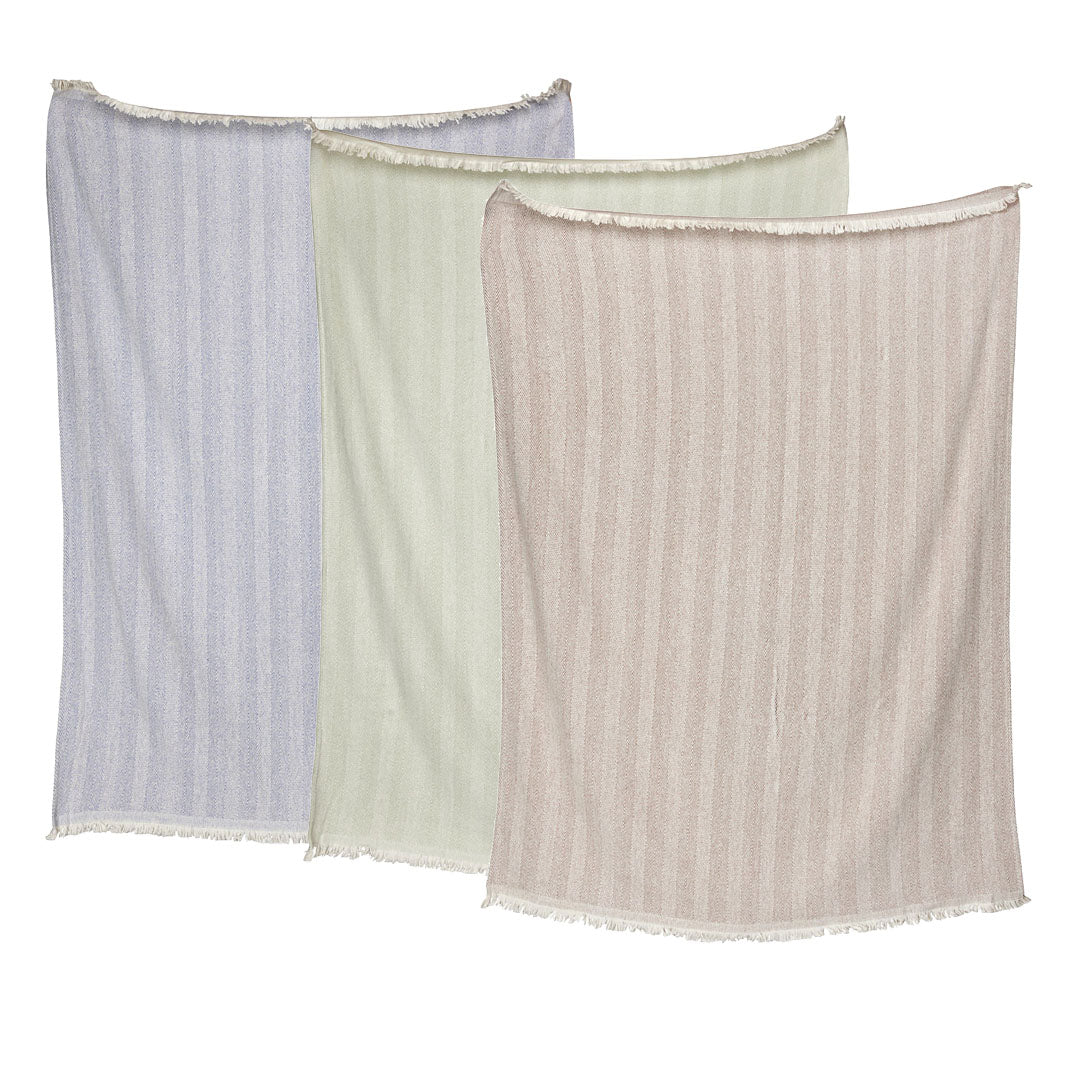 Three striped throws from the John Robshaw Lavanya Throw Collection, in pastel blue, green, and pink, are crafted from yarn-dyed cotton with a subtle herringbone weave and fringe, displayed side by side against a white background.
