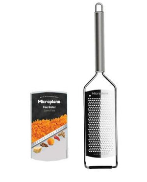 A fine Microplane Professional Series 2.0 Grater Collection tool with a sleek stainless handle sits beside packaging that displays grated cheese and an assortment of spices.
