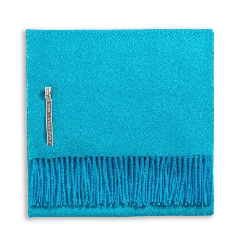Alicia Adams Alpaca's Classic Herringbone Throw Collection: a neatly folded turquoise alpaca blanket with fringe, a fabric label, and fair-trade made in Peru.