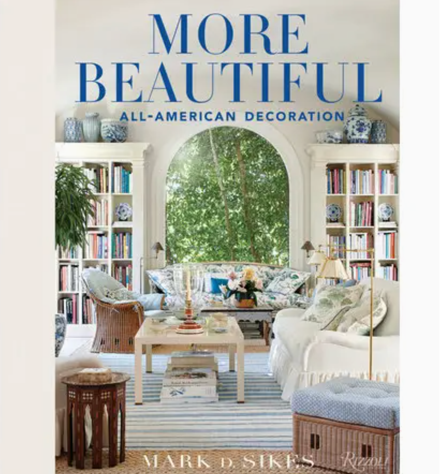 Book cover for “More Beautiful, All American Decoration” by Rizzoli—an inspiring interior design book featuring a bright, elegant living room scene with classic blue and white décor, stylish bookshelves, and a grand arched window that perfectly embodies all-American decorating style.