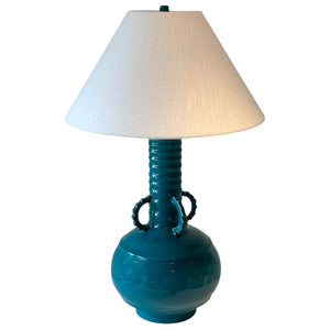 The Ginseng Amphora Lamp in Bermuda by Hwang Bishop features teal ceramic, ornate handles, a ribbed neck, and wide white shade—bringing artful lighting and style to any space.