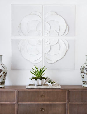 A wooden sideboard with decorative items, including two ornate vases and a small plant in a white ceramic pot, is situated below four pieces of large, 24" square White Flower Quadrant wall art by Tommy Mitchell.