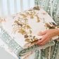 A person holds two folded Vivian Magnolia Floral Scallop Towels from Weezie Towels, featuring a green geometric and floral design, while wearing a green and white patterned garment.