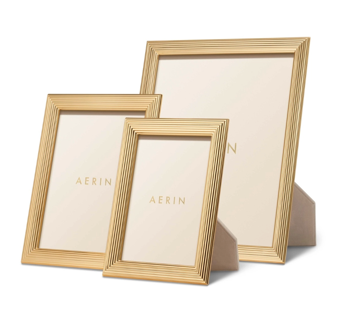 The Alessio Frame Collection by Aerin showcases three rectangular gold frames of assorted sizes with a classic reeded design, standing upright on a white background—perfect for elegantly displaying photographs.