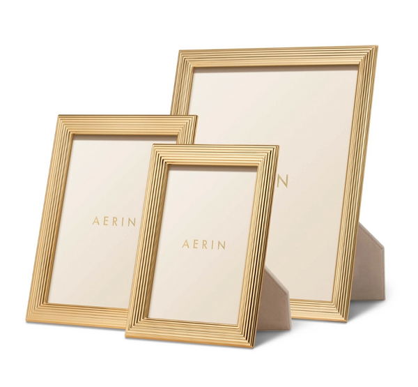 The AERIN Alessio Frame Collection showcases three elegant, gold-rimmed frames of various sizes with a subtle reeded design, each holding a card displaying the brand "Aerin." These upright frames enhance any photograph with their sophisticated style.