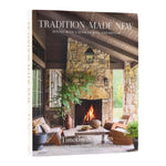 The “Tradition Made New” book from Penguin Random House stands upright, its cover displaying a rustic stone fireplace and cozy seating—an inviting presentation of natural materials that underscores architect Timothy S. Adams’s commitment to timeless craftsmanship.