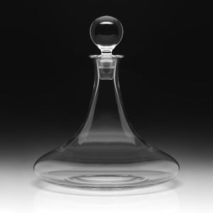 The Trafalgar Ships Decanter by William Yeoward Crystal, featuring a wide base, narrow neck, and round stopper, sits elegantly against a black-and-white backdrop—ideal for serving fine wine or spirits.