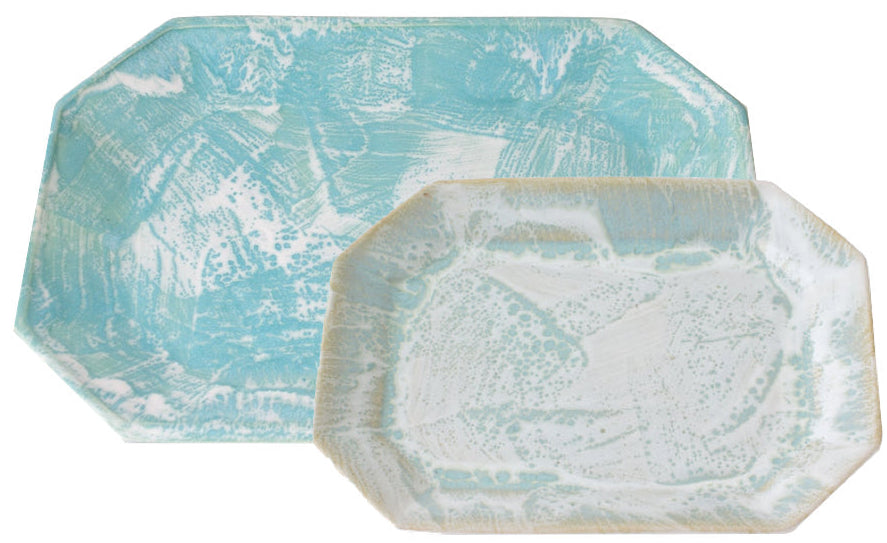 The Brushstroke Tray Collection by Paul Schneider Ceramics features two overlapping rectangular ceramic platters—one light blue, one white—with angled corners and refined glazes for an elegant display.