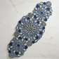 The Marisol Runner, Blue/Natural by Kim Seybert adds artisanal style to your table with its intricate patterns, beautifully displayed diagonally on a subtly veined light marble surface.