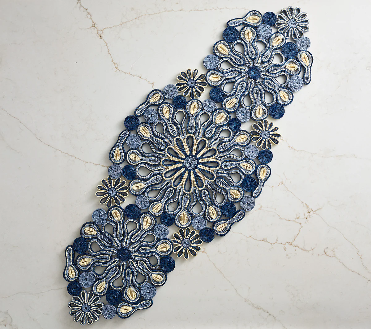 The Marisol Runner, Blue/Natural by Kim Seybert adds artisanal style to your table with its intricate patterns, beautifully displayed diagonally on a subtly veined light marble surface.