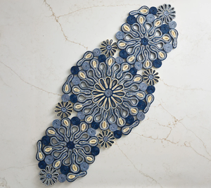 The Marisol Runner, Blue/Natural by Kim Seybert adds artisanal style to your table with its intricate patterns, beautifully displayed diagonally on a subtly veined light marble surface.