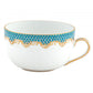 A white porcelain teacup from Herend’s Fish Scale Turquoise Collection features a gold rim and handle with a blue and gold scalloped pattern, echoing the hand-painted elegance of Herend dinnerware.