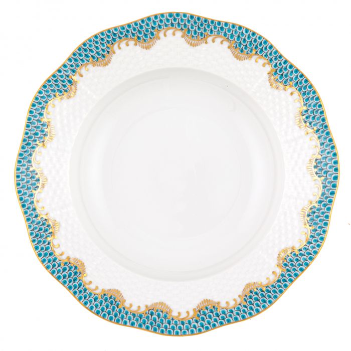A round white porcelain plate with a textured center and a scalloped rim featuring blue and gold patterns, inspired by Herend's Fish Scale Turquoise Collection.