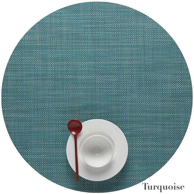 A white cup and saucer with a red spoon sit on a Chilewich Round Placemat in turquoise, made from phthalate-free Terrastrand yarns. The word "Turquoise" appears in the lower right corner.