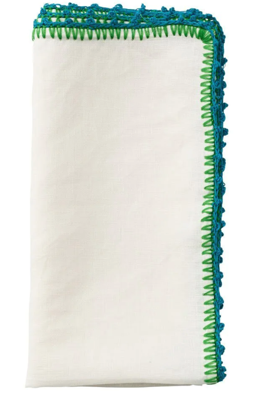 The Kim Seybert Knotted Edge Napkin Set features folded white 100% linen napkins with green and blue hand-crocheted edging.