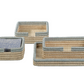 The La Côte Coiled Napkin Holder Collection by Zodax features three rectangular woven trays with beige and grey edges, stacked or side by side—ideal for displaying coasters and elevating your coastal table décor.