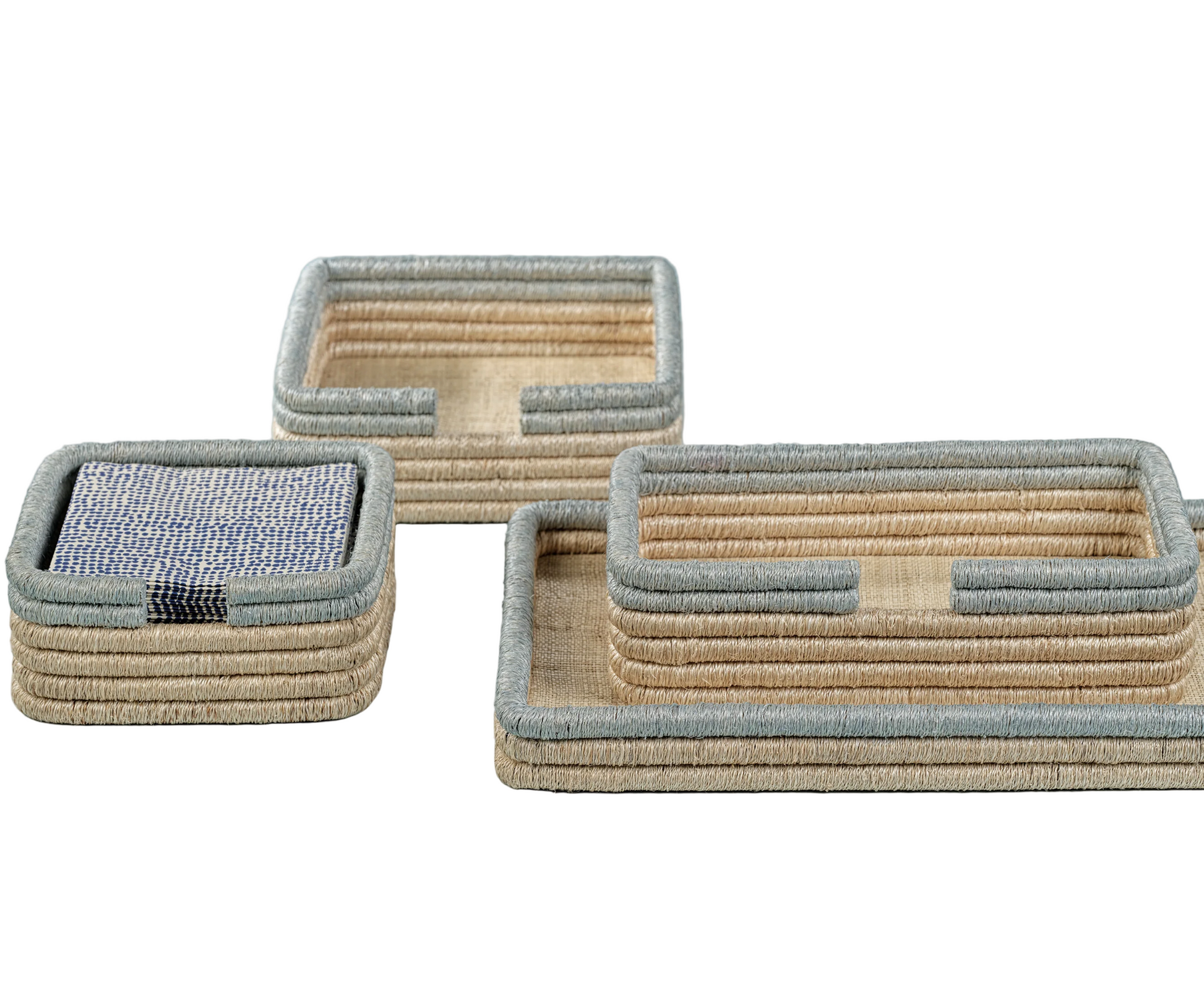 The La Côte Coiled Napkin Holder Collection by Zodax features three rectangular woven trays with beige and grey edges, stacked or side by side—ideal for displaying coasters and elevating your coastal table décor.