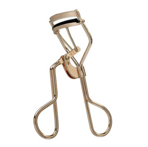 The Tweezerman Curl 38 Eyelash Curler is a gold metal curler with black rubber padding, designed to enhance almond-shaped eyes, shown against a white background.