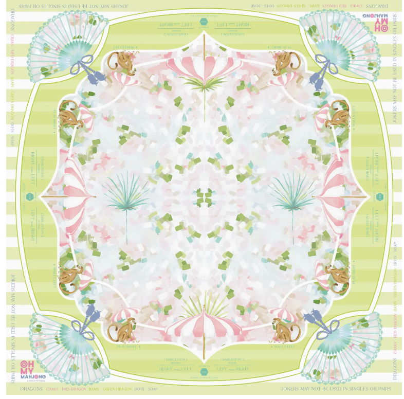 The Oh My Mahjong Mahjong Mat Collection features a square scarf with a pastel symmetrical design of squirrels, fans, and green and pink accents. Inspired by a Mahjong mat, it has striped green edges and border text on a non-slip surface.