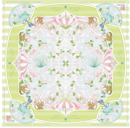 The Oh My Mahjong Mahjong Mat Collection features a square scarf with a pastel symmetrical design of squirrels, fans, and green and pink accents. Inspired by a Mahjong mat, it has striped green edges and border text on a non-slip surface.