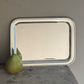 A Vintage Oblong Tray by Hôtel Silver stands upright against a wall on a wooden surface, with a green pear placed in front of it.