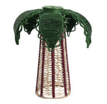 The Palm Candle Holder & Flower Vase by Mercedes Salazar is a handcrafted piece featuring a woven reed design with a conical base and green, leaf-like fronds reminiscent of a stylized palm tree, artfully adorned with raffia fiber for a natural, artisanal accent.