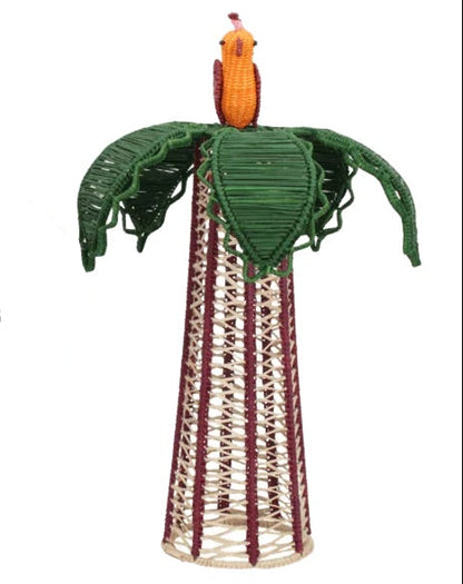 The Hoatzin Palm Candle Holder & Flower Vase by Mercedes Salazar features a woven sculpture of a bird perched atop green leaves, set on a conical base crafted from interlaced natural and maroon fibers—an exquisite piece of handcrafted dining decor.