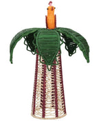 The Hoatzin Palm Candle Holder & Flower Vase by Mercedes Salazar is a handcrafted woven sculpture featuring a cone-shaped base, green leaves, and an orange figure reminiscent of a bird or fruit at the top. This exquisite piece serves as artisanal dining decor, perfect for placing atop a table or beside a natural raffia vase to bring warmth and charm to any setting.