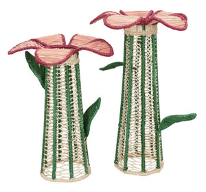 Two tall Lily Floral Spirit Candle Holder & Flower Vases by Mercedes Salazar—handcrafted from natural raffia fiber in the brand’s signature style—feature woven designs resembling blooming flowers, with pink tops and green stems and leaves.