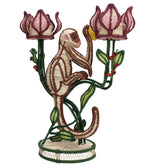 The Jungle Whisper Mico Candle Holder by Mercedes Salazar showcases a hand-embroidered monkey climbing green stems, topped with two pink flower-shaped candle holders—melding artisanal raffia techniques with the brand’s distinctive creative flair.