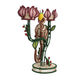 The Jungle Whisper Mico Candle Holder by Mercedes Salazar features a handwoven raffia elephant figurine standing amid three pink flowers with green stems, all crafted from colorful thread on a circular base—an enchanting example of artisanal decor.