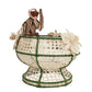 The Forest Muse Mono Bowl by Mercedes Salazar is a handcrafted raffia décor bowl with green accents, adorned with a brown monkey figure and beige butterfly shapes attached to the rim—a whimsical piece designed in Bogotá, Colombia.