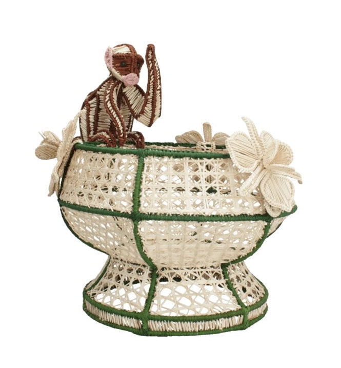 The Forest Muse Mono Bowl by Mercedes Salazar is a handcrafted raffia décor bowl with green accents, adorned with a brown monkey figure and beige butterfly shapes attached to the rim—a whimsical piece designed in Bogotá, Colombia.