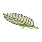 The Frog Leaf Amazonas Tray by Mercedes Salazar features an embroidered patch of a green leaf with a small green lizard beneath it, echoing the natural motifs found in handwoven raffia fiber trays, set against a plain white background.