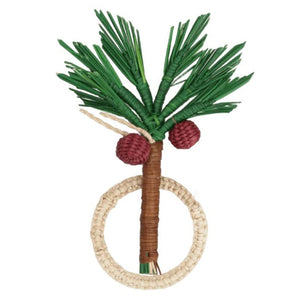 The Coconut Palm Tree Napkin Ring by Mercedes Salazar is handmade in Colombia from natural raffia fiber and features green palm leaves, two red fruits, and a brown trunk attached to a beige circular ring—an exquisite example of the brand's signature napkin rings.