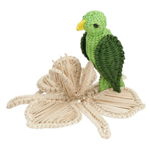 A small woven green bird with a yellow beak perches on a beige palm leaf crafted from raffia fiber, capturing the exquisite handmade style of Colombia in the Mercedes Salazar Pajarito Napkin Ring.